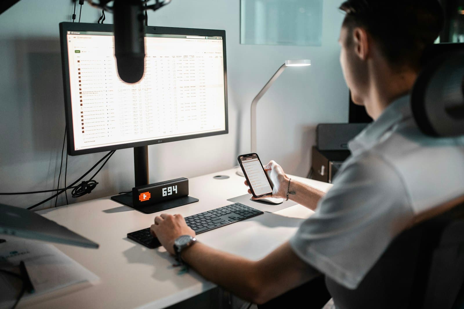 Person reviewing campaign data on a monitor while holding a phone, representing message cost optimization and analytics.